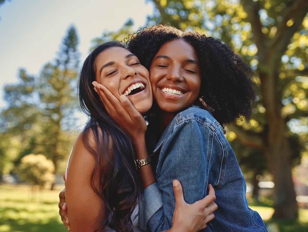 Two women smiling and embracing outdoors